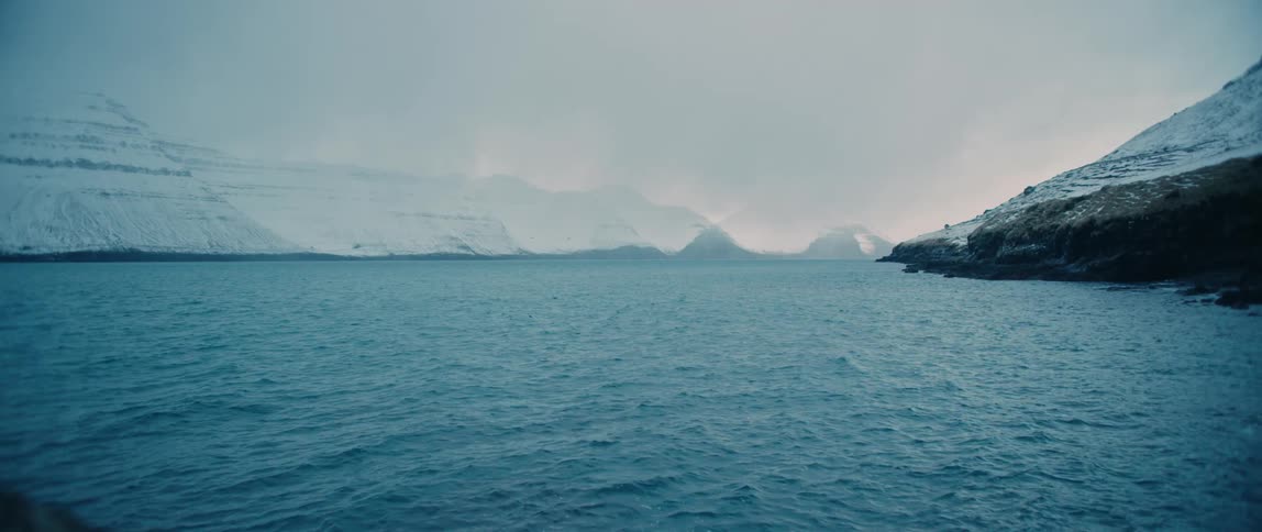 Placid scene of a river next to snow covered mountains at evening