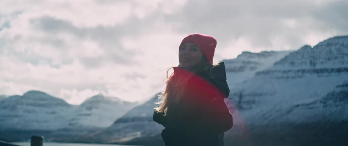 Smiling woman runs at side of road across water from snow covered mountains on an overcast day