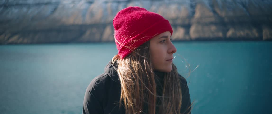 Woman adjusts red beanie standing outdoors in front of ocean cliffs