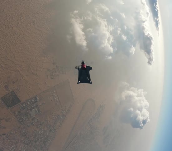 Someone wearing a wingsuit to glide above the clouds slowly falling towards the ground