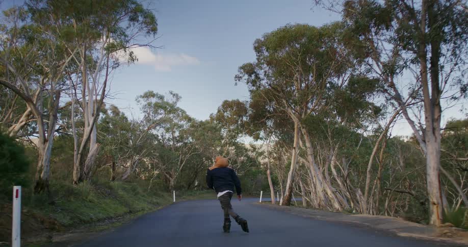 Man with his back turned rollerblading on a road amidst a treelined vegetation