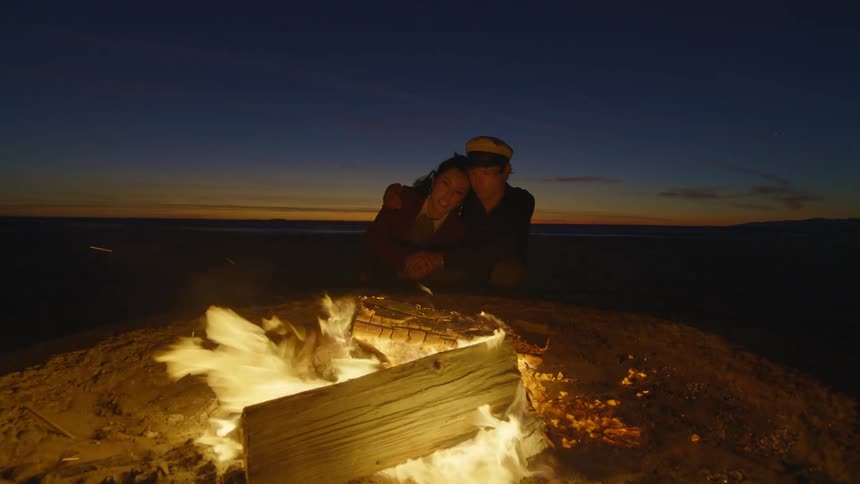 A man and a woman are holding each other next to a fire on the beach
