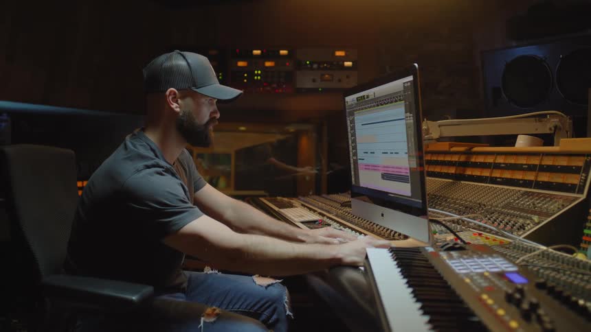 A man sitting is playing on a screen and next to him there is an electric piano