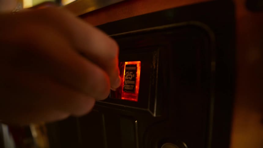 Closeup of a persons hand inserting a coin into an arcade game machine