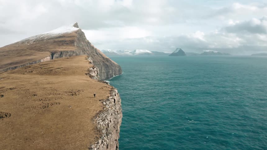 Aerial of person running on the edge of a cliff near the ocean
