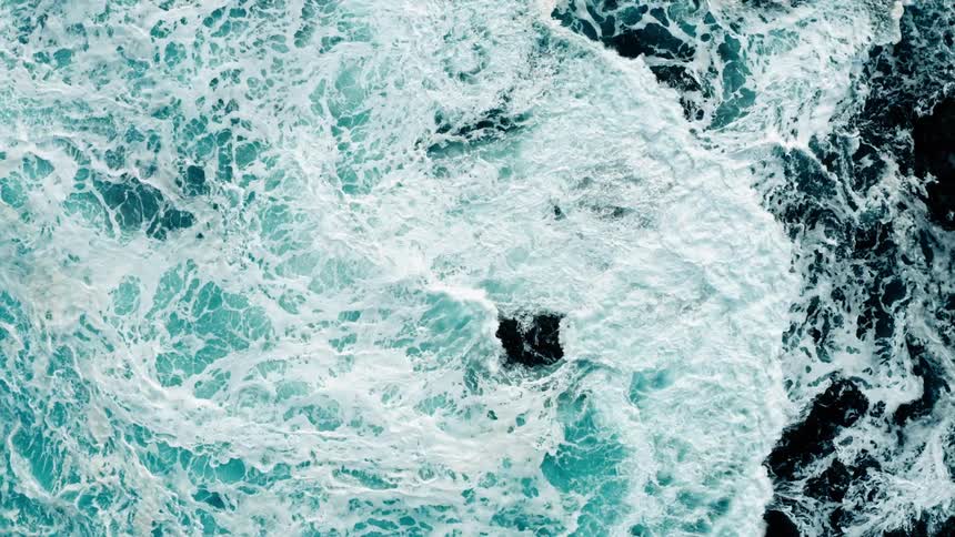 Aerial of the rough sea with waves breaking on the rock