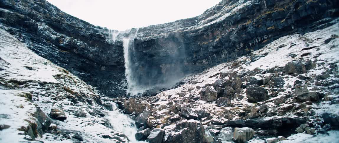 A waterfall of water from a huge rock that fell onto several small rocks that are covered in snow