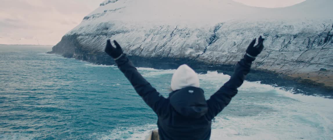 A woman raises her arms by the shore
