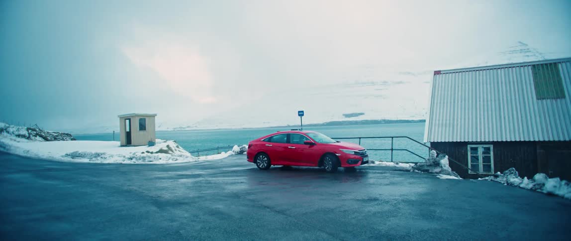 Red car parked on a street by the seaside with the ground covered in snow