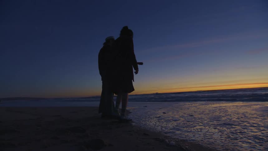 Man and woman standing by the sea is silhouetted against the sunset on the beach