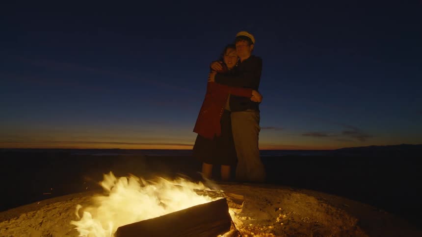 Young couple hug in front of a bonfire at the beach