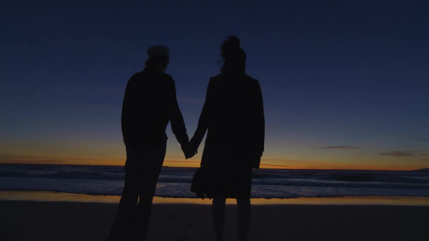 A couple holding hands standing by the sea during dusk