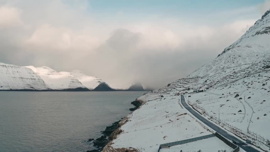 Aerial panorama of a village by a lake surrounded by a mountain range covered in snow