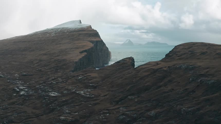 Patches of snow cover terrain leading to seaside cliff on a foggy day