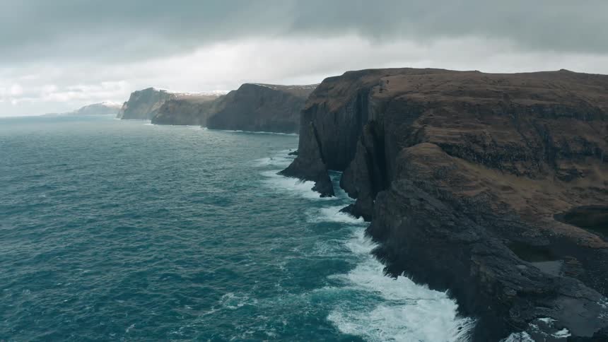 Aerial view of ocean waves breaking against cliff and coastline