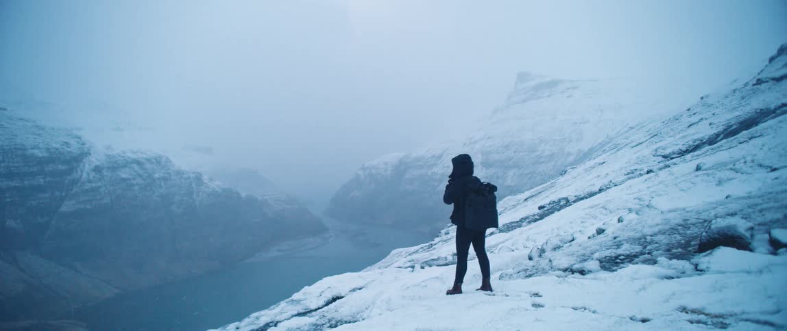 Person trekking on a snowcovered mountain with a lake at the edge