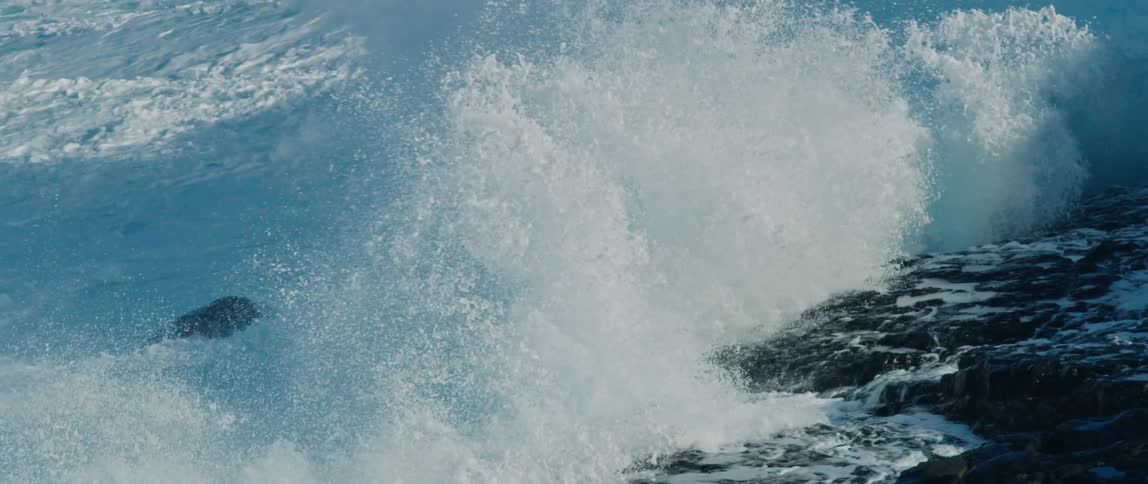 Violent waves crash onto the rocky shore during the day