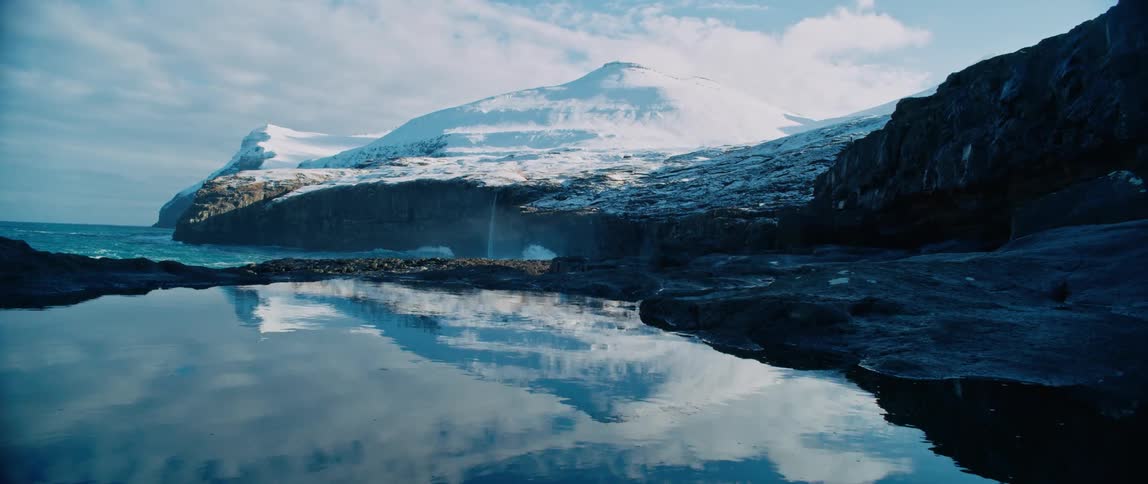A mountain range with snow and sea waves crashing on the beach