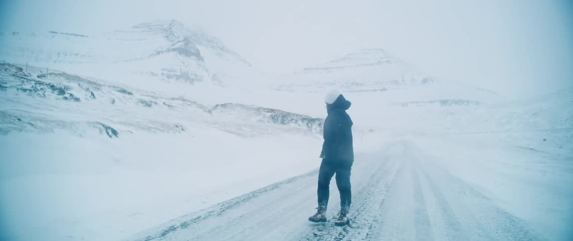 Person walking on a road holding a camera during a snowstorm