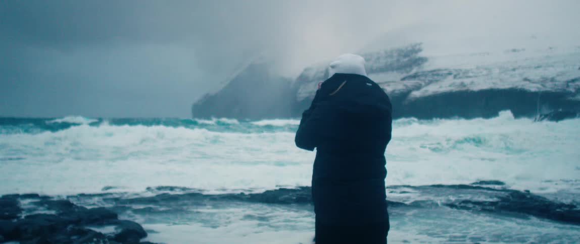 A person photographing the seascape with snowcapped mountains