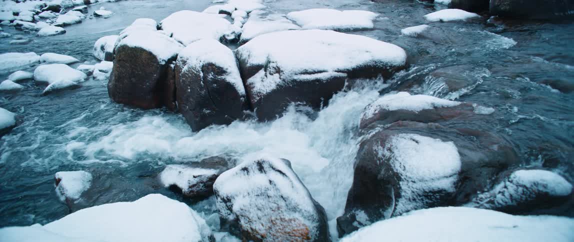 A small stream that leads to several rocks covered in snow