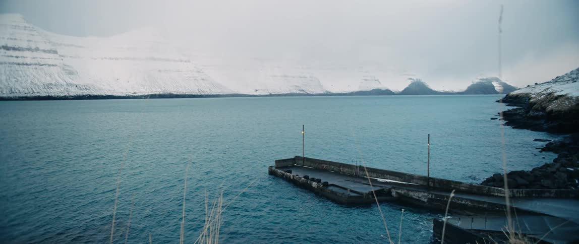 Small pier on a lake next to snow covered mountains
