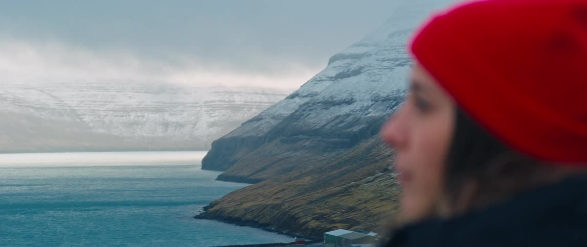 Woman in a red hat turns head overlooking the sea and mountains