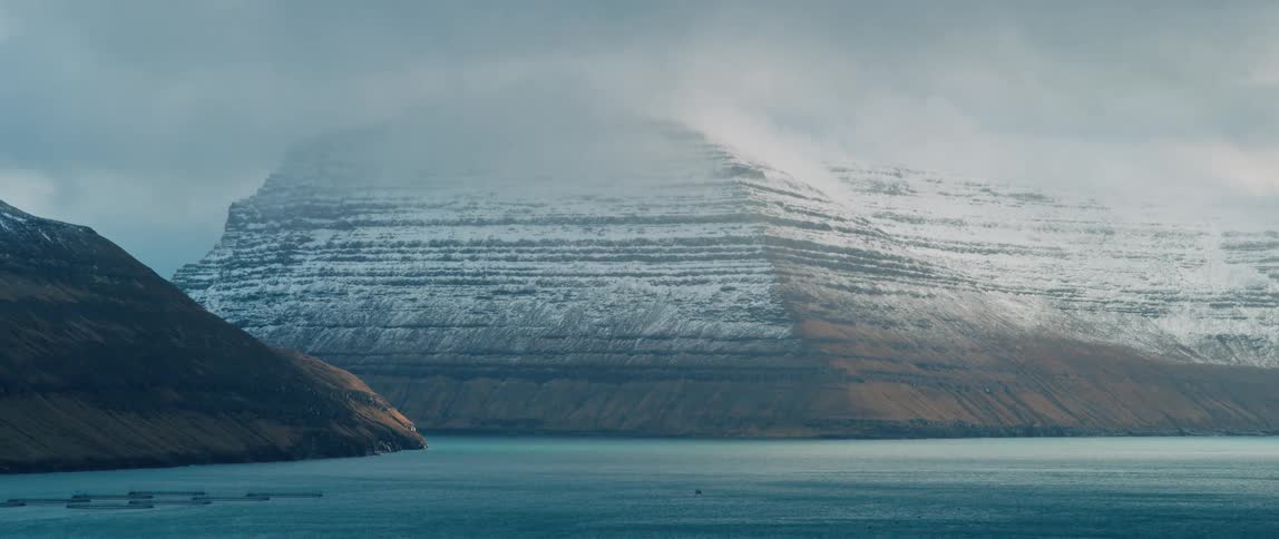 A large mountain with snow and its top covered by a cloud faces the sea