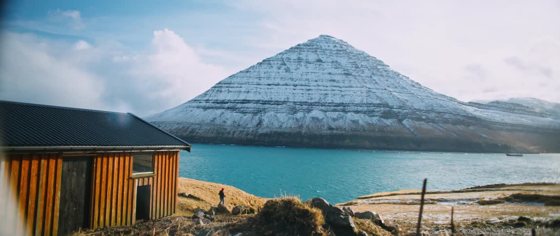 A person walks by the water near a cabin