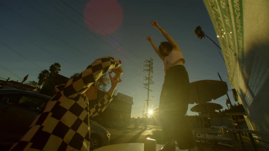 Woman dancing on a table outside with another man beside her signaling and dancing along