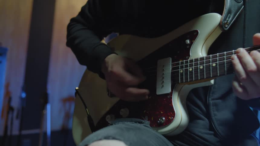 A man is sitting and is playing an electric guitar and shaking his head