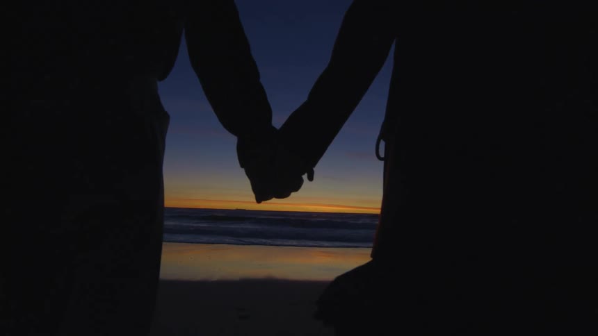 Silhouette of a couple walking hand in hand towards the sea on the beach with a dawn sky