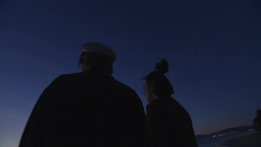 A couple is holding hands and standing on the beach watching the sea
