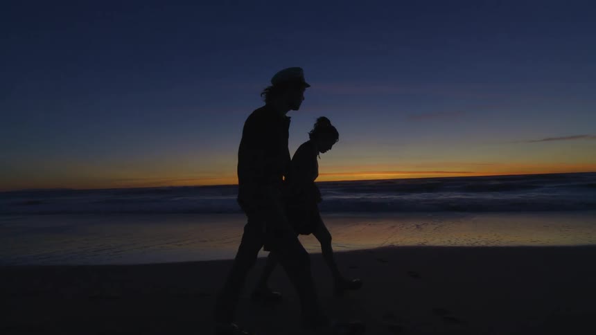 A couple walking hand in hand on the beach at dusk