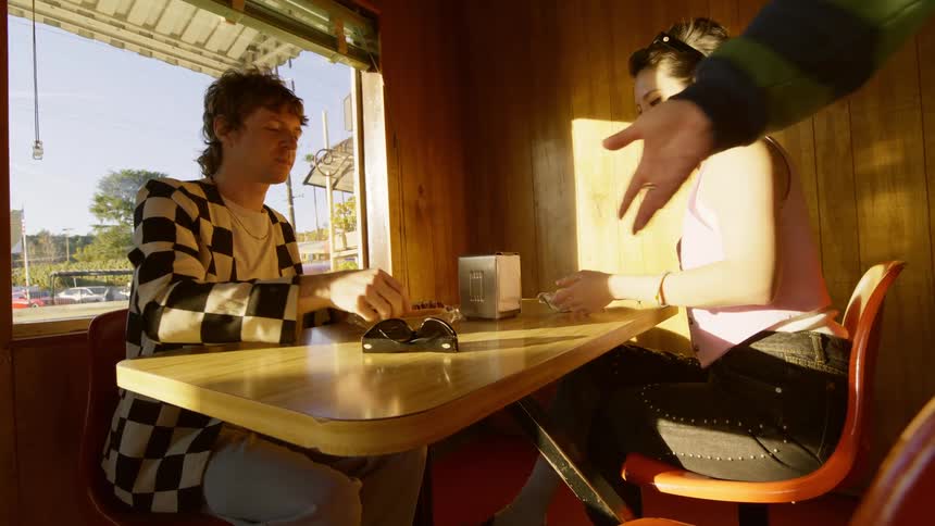 A man places two hotdogs on the table serving a couple on a date