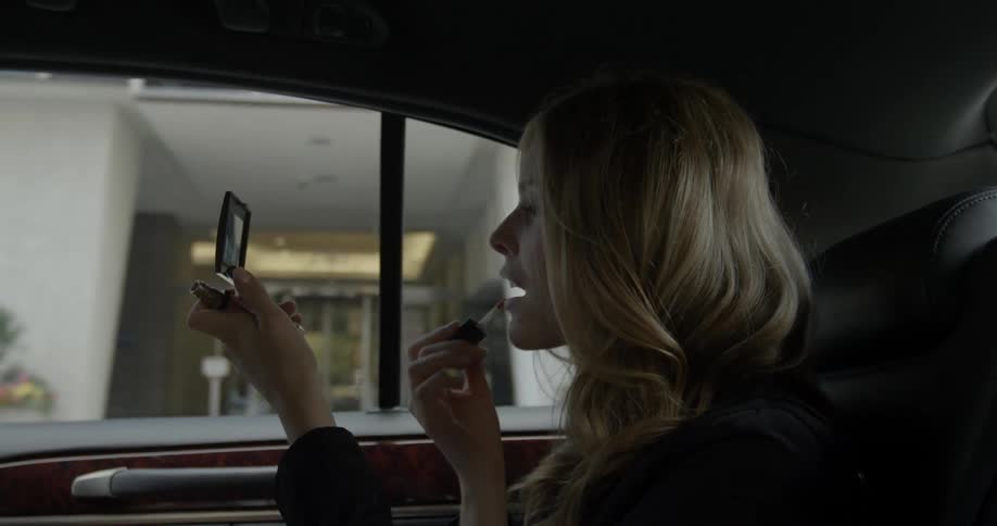 A woman is putting on makeup in the back of a moving car