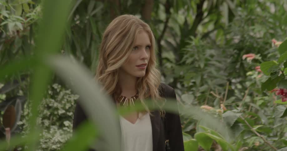 A woman in a large gold colored necklace walking through a garden