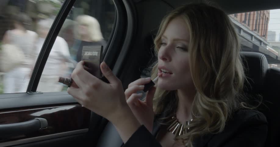 Woman applies lip gloss while riding in car