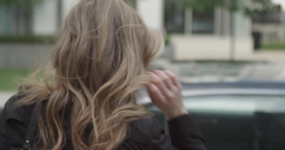 Woman walking towards and getting into car on windy day