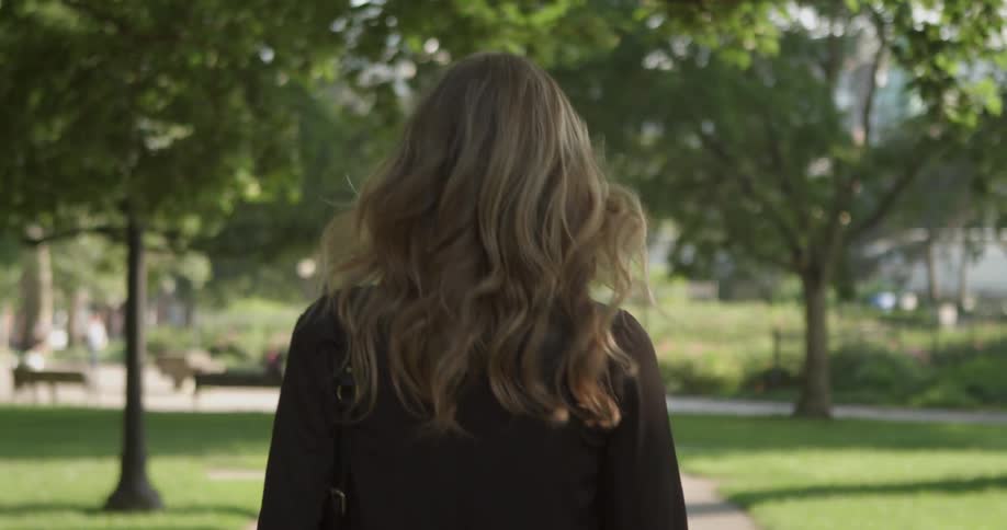 A blonde woman walks down the sidewalk in a park