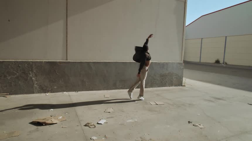 Black man dances during the day near industrial warehouse