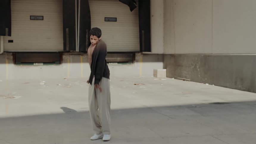 Male dancer wearing a brown shirt and beige pants dances in the warehouse