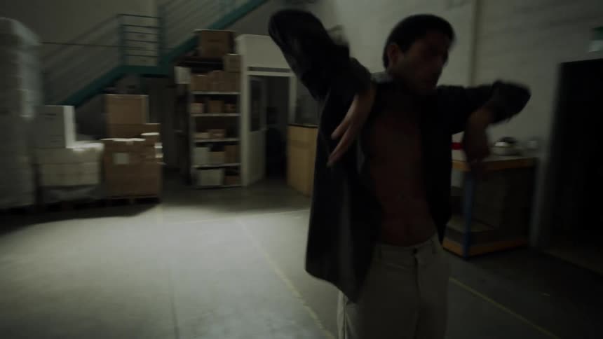 Man with a brown short and gray pants dances in a warehouse