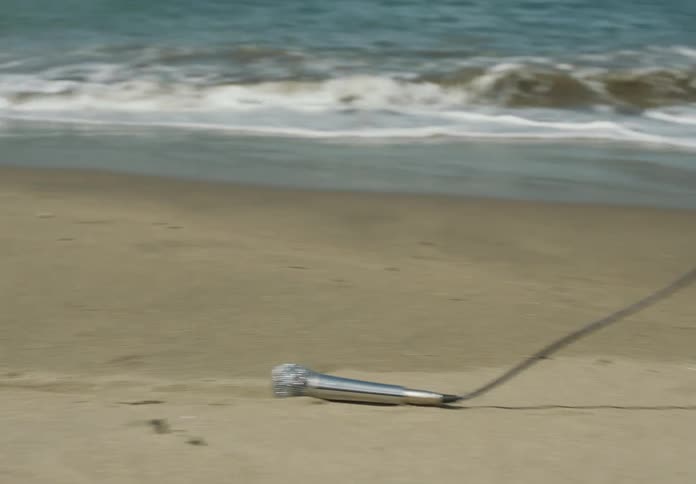 A microphone is dragged by its cord through the sand near the ocean