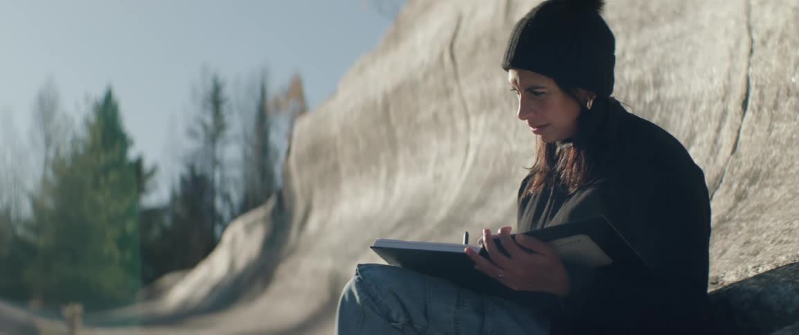 Woman sits in a granite rock formation writing in a notebook