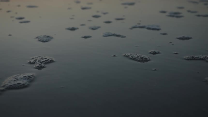 View of wet sea sand with foam and bubbles on a morning