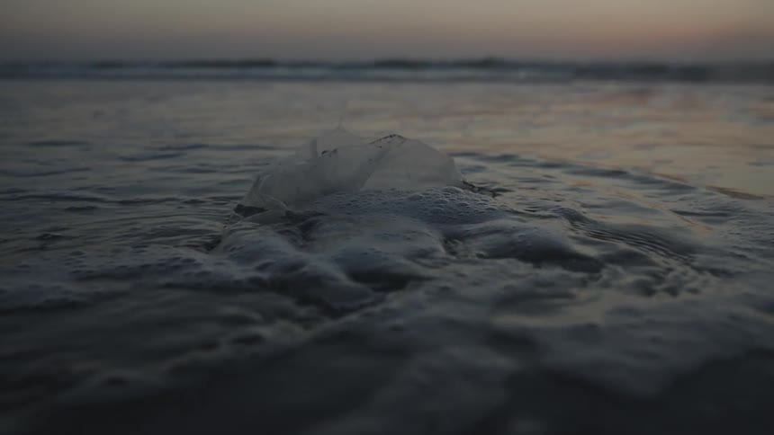 Bag thrown on the beach sand with seawater passing in slow motion on a morning