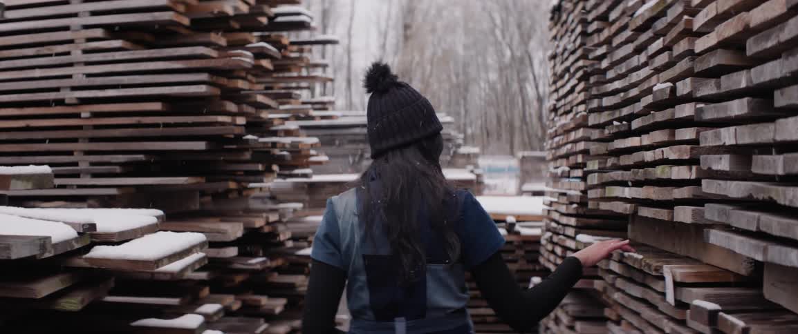 A woman touches the wood in a lumber yard as it snows