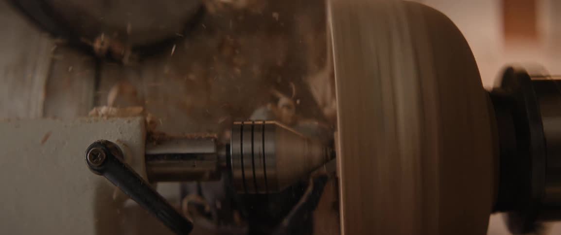 A woman uses a lathe for shaving pieces of wood out of a sculpture in slow motion