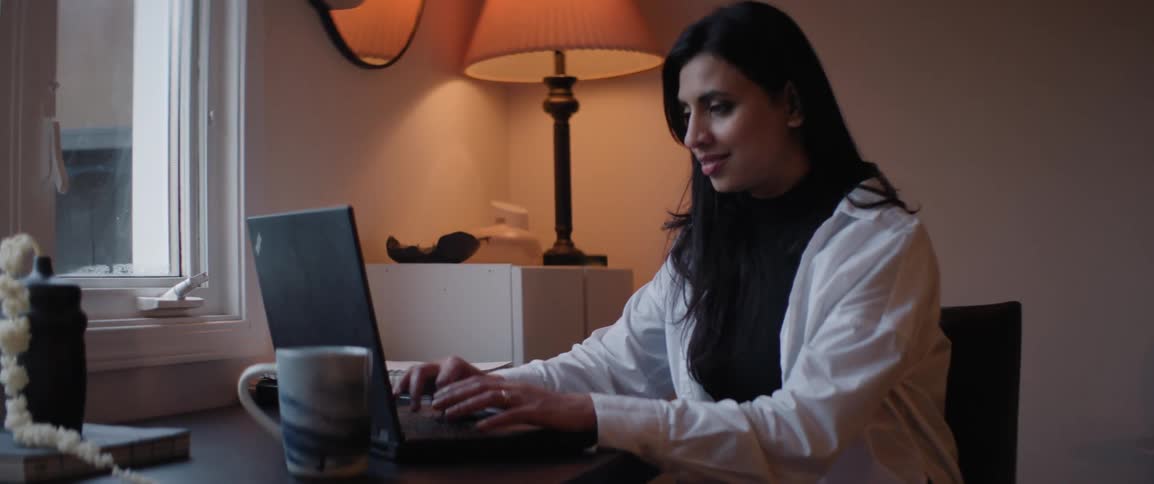 Smiling woman sits typing on laptop near window
